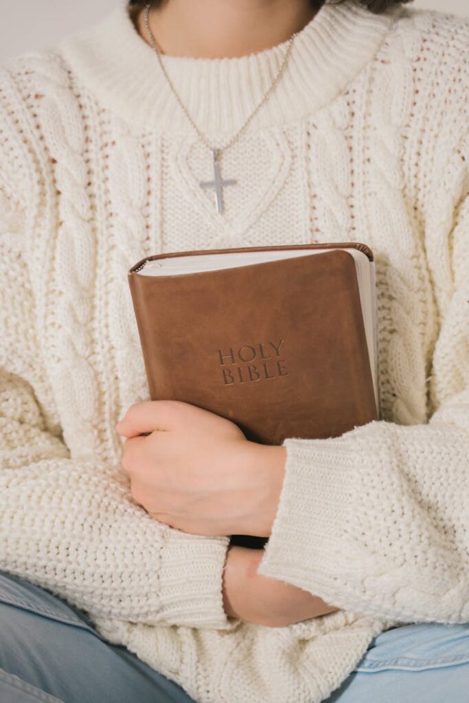 pexels photo 5199754 An individual in a knitted sweater holds a Holy Bible and wears a cross necklace, symbolizing faith.